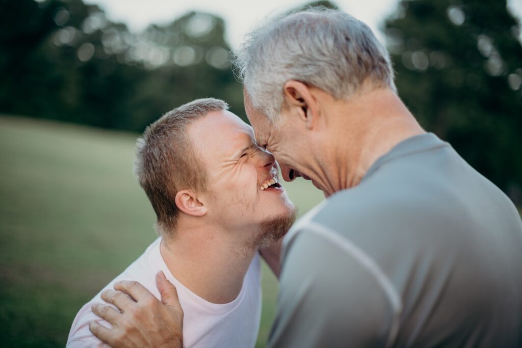 Older man with a younger man smiling with heads close to one another