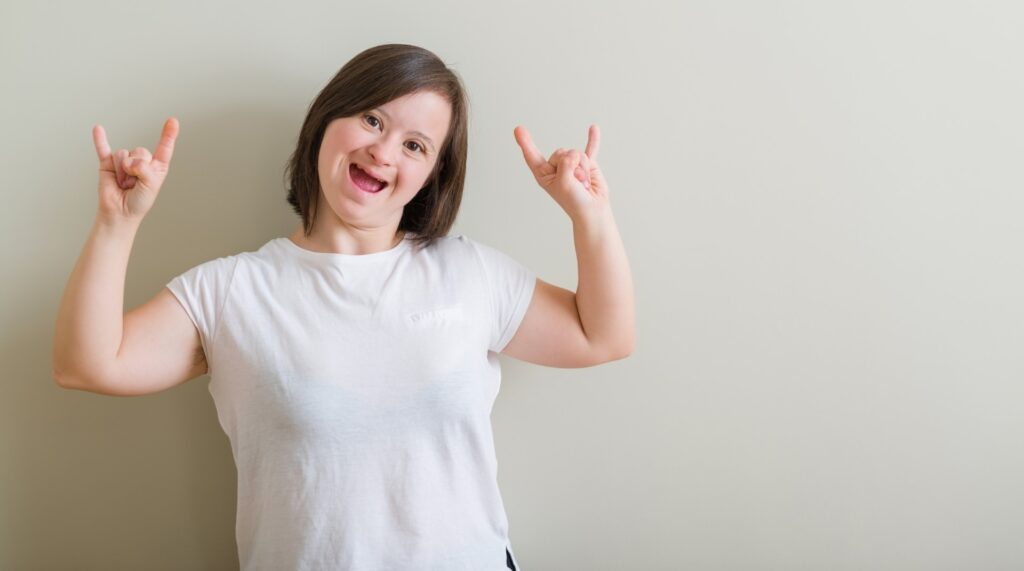 Down syndrome woman standing over wall shouting with crazy expression doing rock symbol with hands up. Music star. Heavy concept.